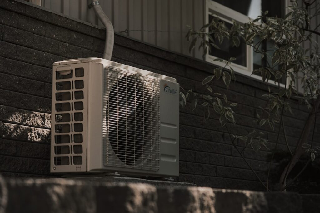 A technician examines an outdoor air conditioning unit next to a home on a sunny day.